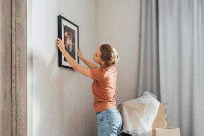 Young woman putting picture frame on wall at new home